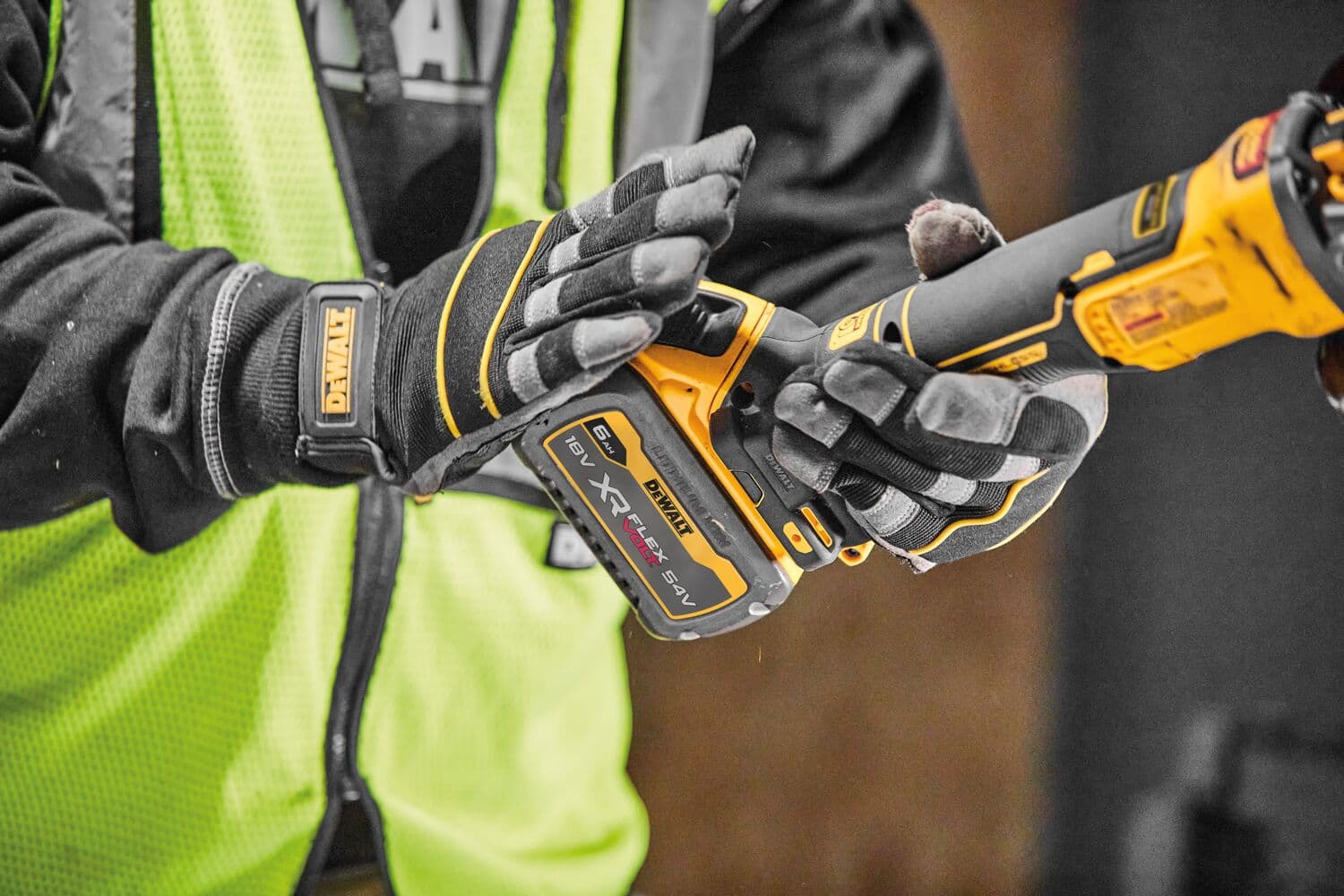 Person with gloves holds a DEWALT cordless XR FLEXVOLT power tool, wearing a yellow safety vest.
