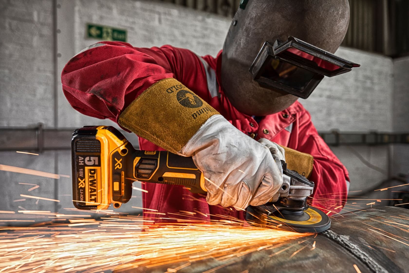 A person wearing protective gear uses a DEWALT cordless angle grinder (DCG405) to grind metal, producing sparks.