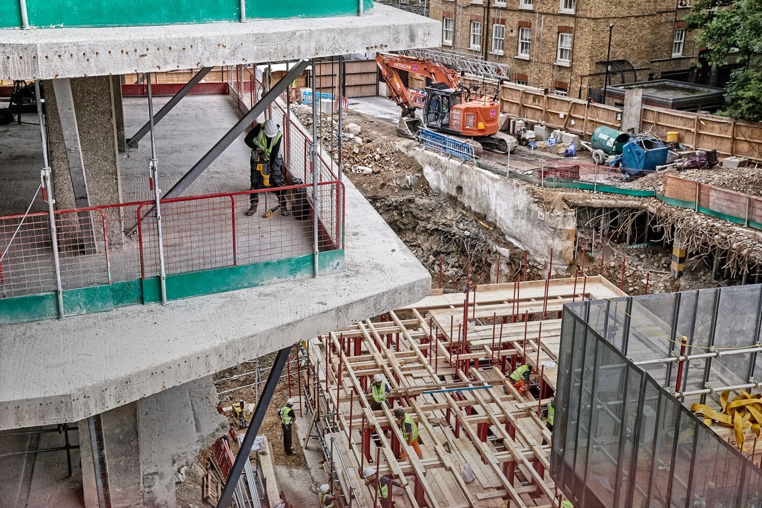 Construction site with workers, concrete structures, scaffolding and excavator in an urban area.