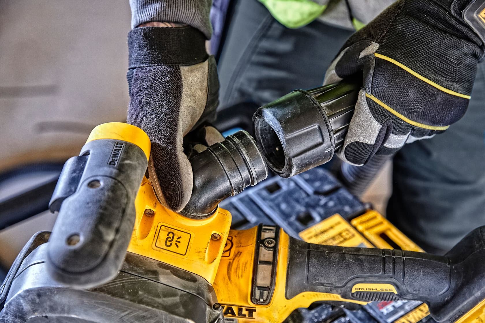 Gloved hands attach a hose to a yellow DEWALT power tool, shown in close-up during use.