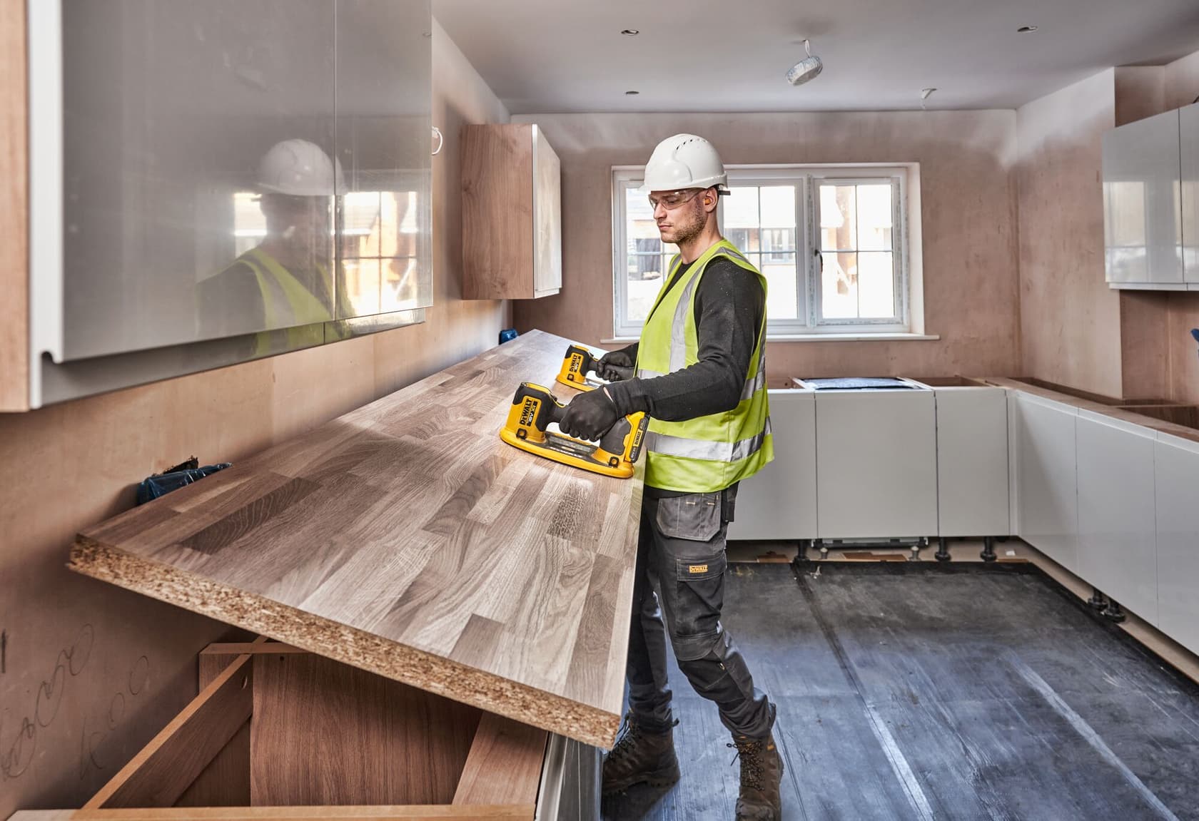 Worker uses DEWALT DCE590 tool to install a wooden countertop in a kitchen under construction.