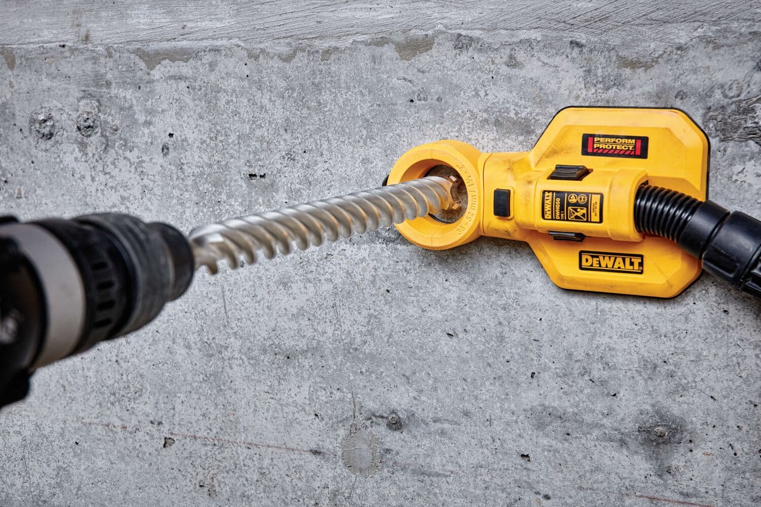 A DEWALT dust extraction attachment is being used with a rotary hammer drill to drill into a concrete wall. The attachment collects dust while drilling, helping to keep the workspace clean.