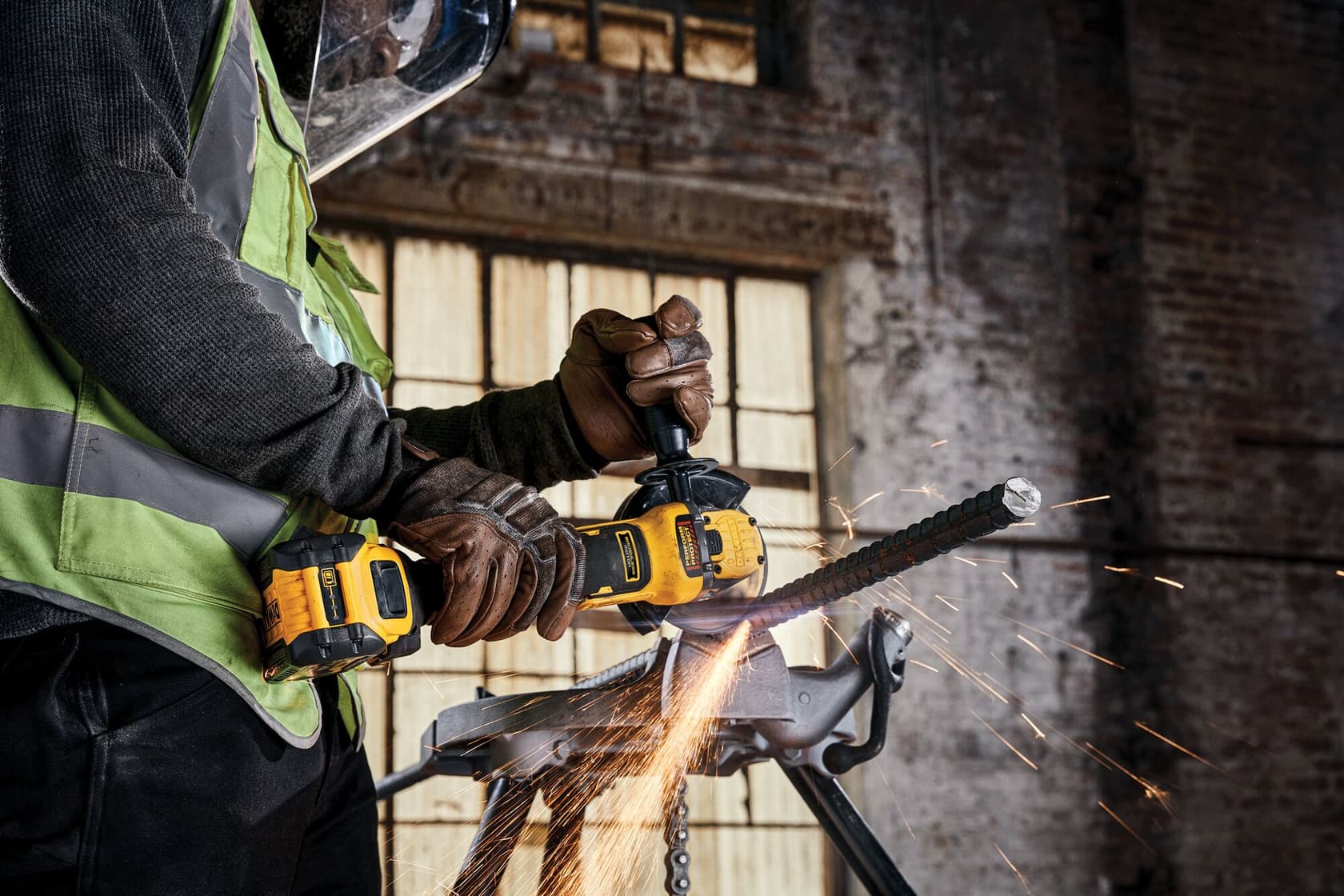 Worker uses DEWALT cordless angle grinder to cut metal rebar, sparks flying at industrial jobsite.