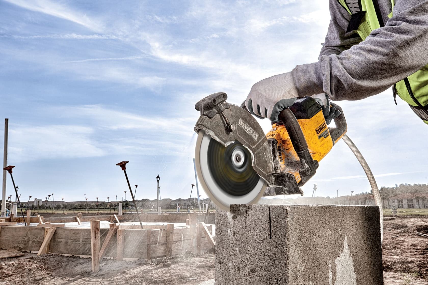 Person cutting concrete block outdoors with DEWALT power saw; dust and debris visible.