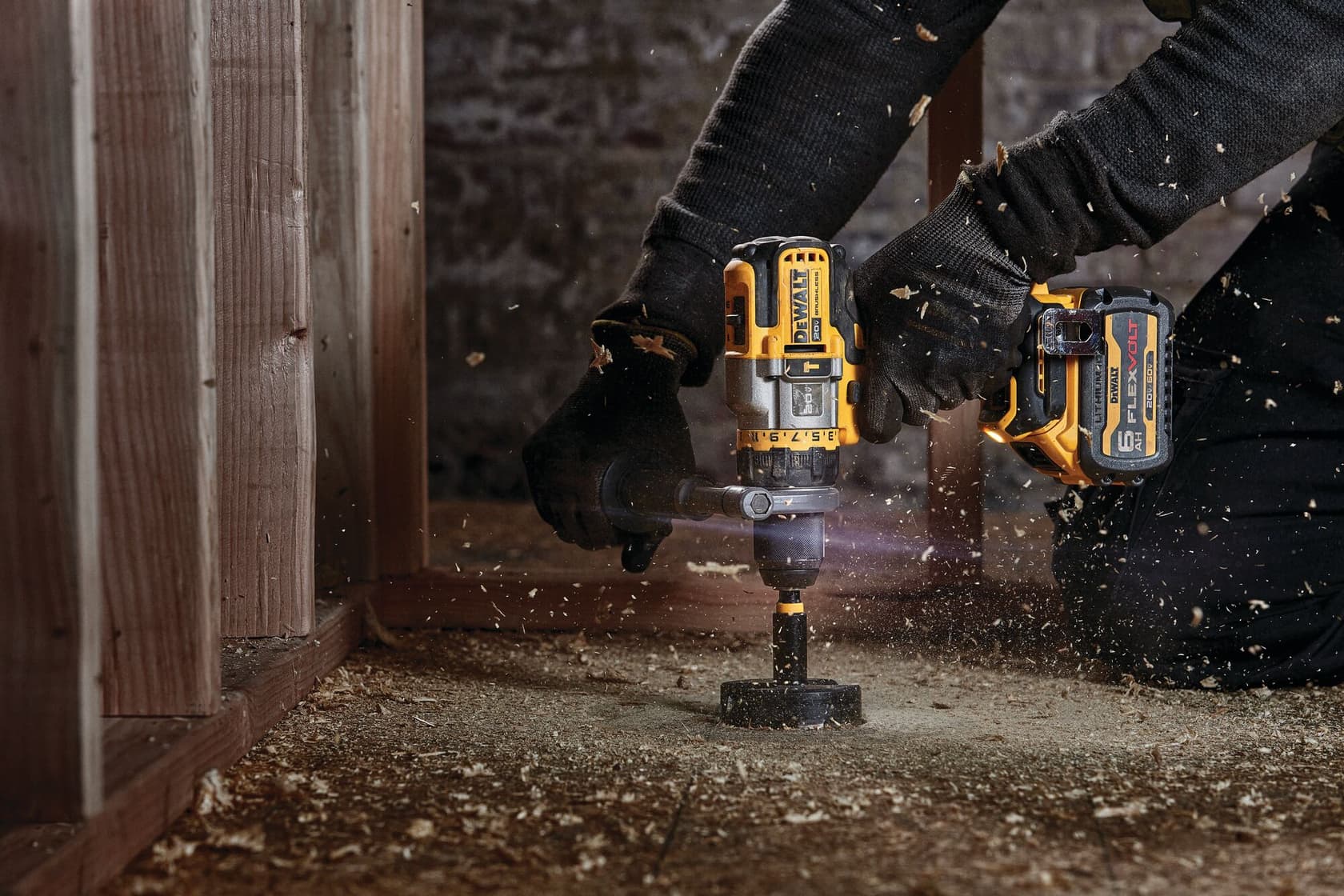 Person uses a DEWALT cordless drill to bore a hole in wood, with sawdust and debris flying around.
