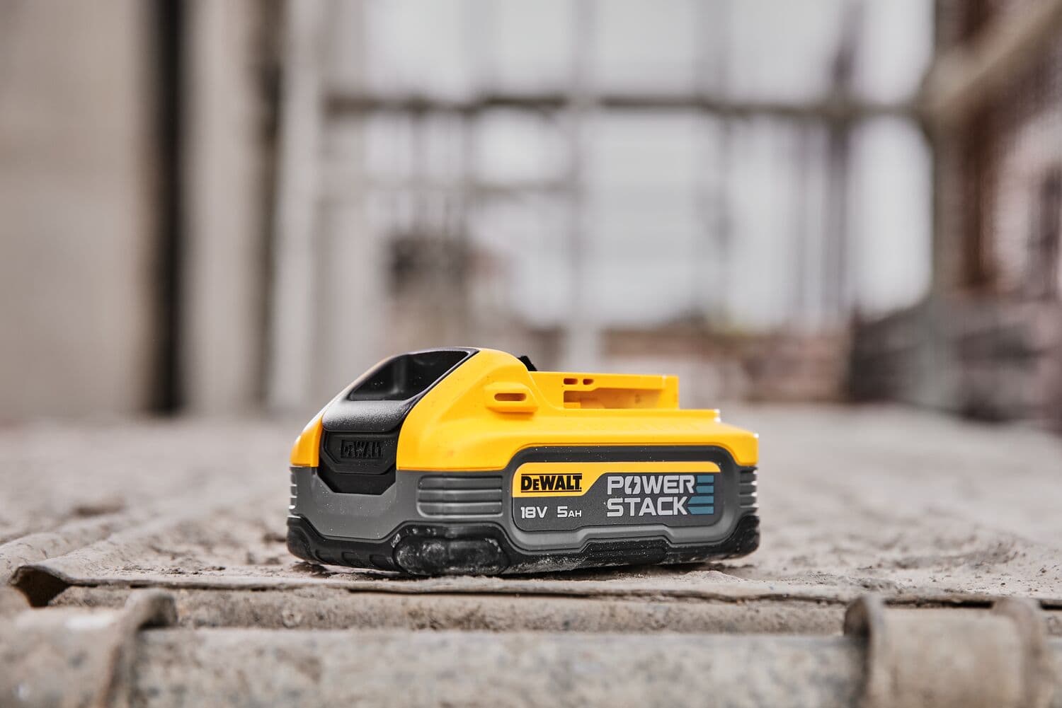 DEWALT POWERSTACK 18V 5Ah battery shown on a concrete surface in an industrial setting.