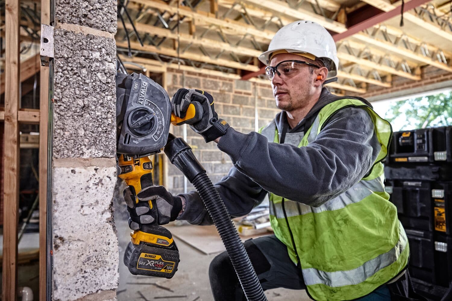Worker uses DEWALT DCG200T2 wall chaser tool on concrete wall at construction site, wearing safety gear.