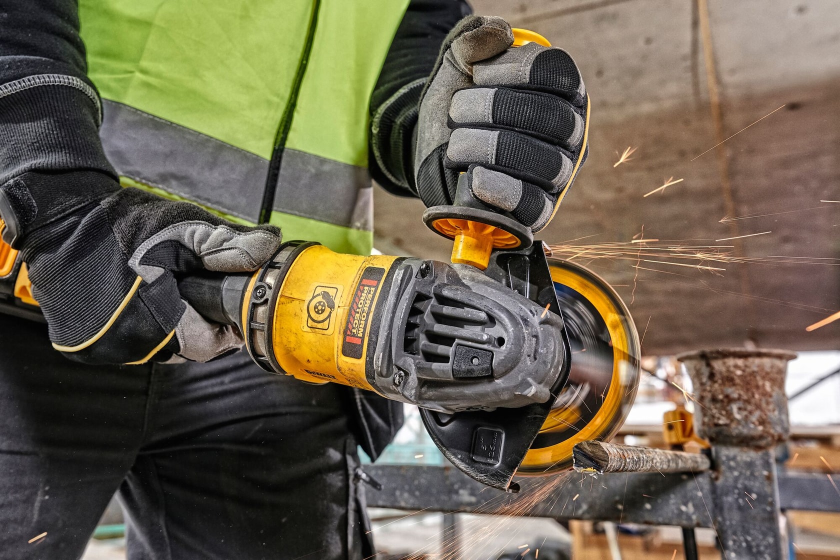 Person using a yellow DEWALT angle grinder to cut metal, sparks flying, wearing gloves and safety vest.