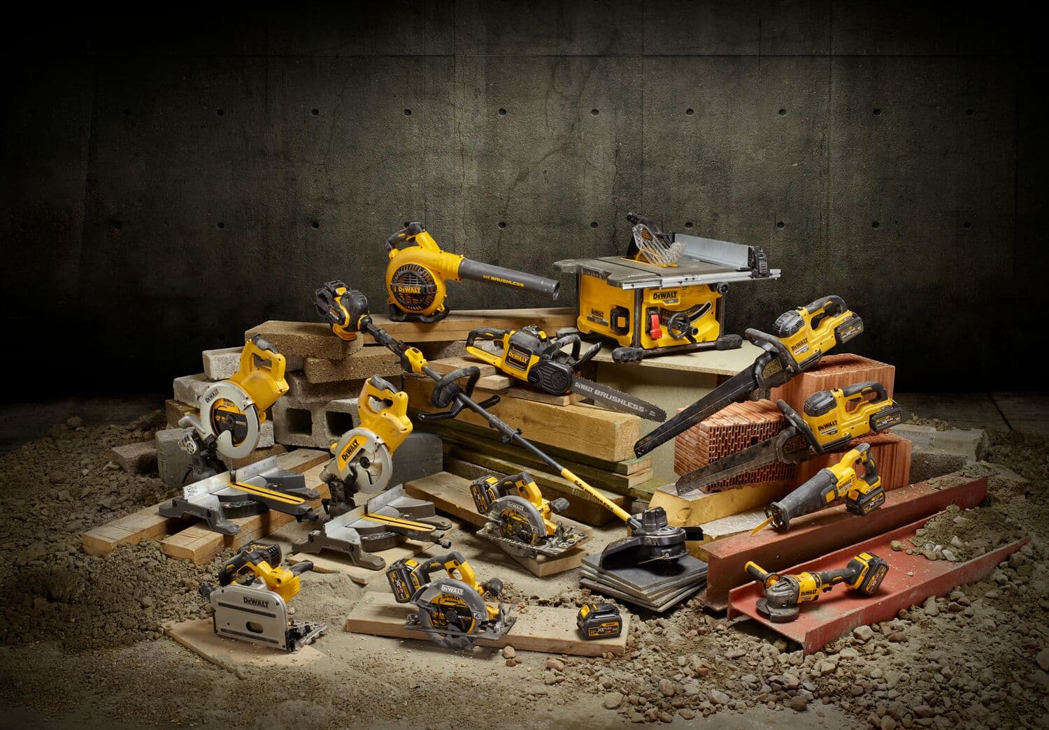 A collection of yellow and black DEWALT power tools is displayed on a pile of bricks and wooden planks in a workshop setting. The tools include saws, drills, a blower, and other equipment.