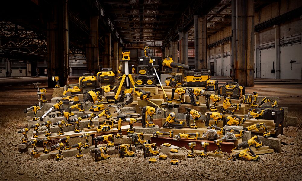 A large assortment of DEWALT power tools and accessories, including drills, saws, grinders, and toolboxes, are arranged on concrete blocks in an industrial warehouse setting.